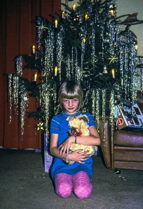 Ein Kind mit einem Teddybär, knieend vor einem Weihnachtsbaum